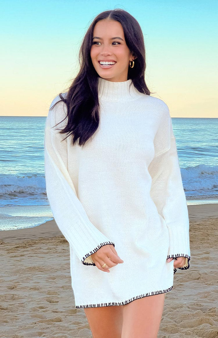 Close-up of the cream knit sweater dress showing the high neck and black contrast trim on the cuffs and hem