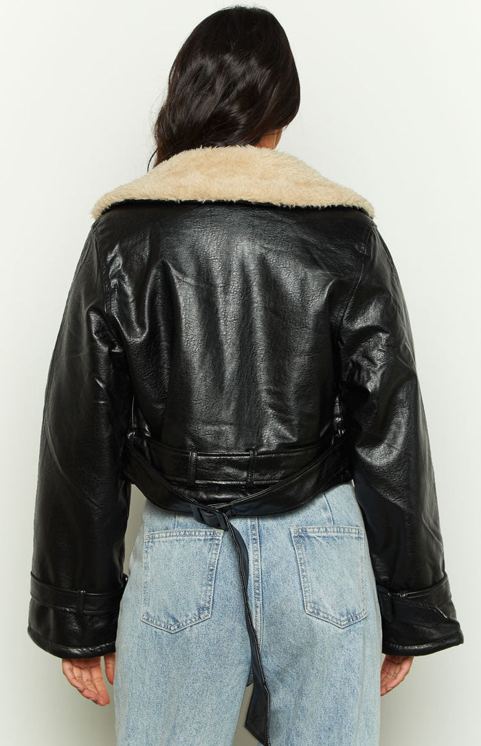 Back view of a black faux leather cropped jacket with a cream faux fur collar and a long tie-waist belt