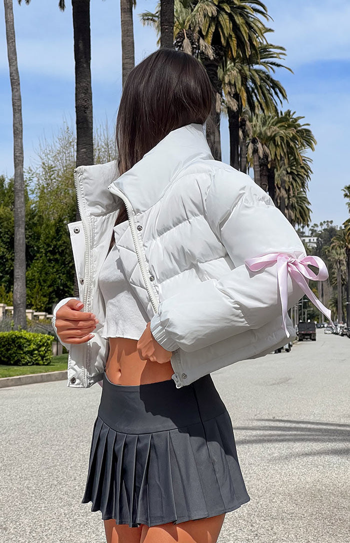 Side view of a white cropped puffer jacket with a high stand collar and pink bow detail on the sleeve