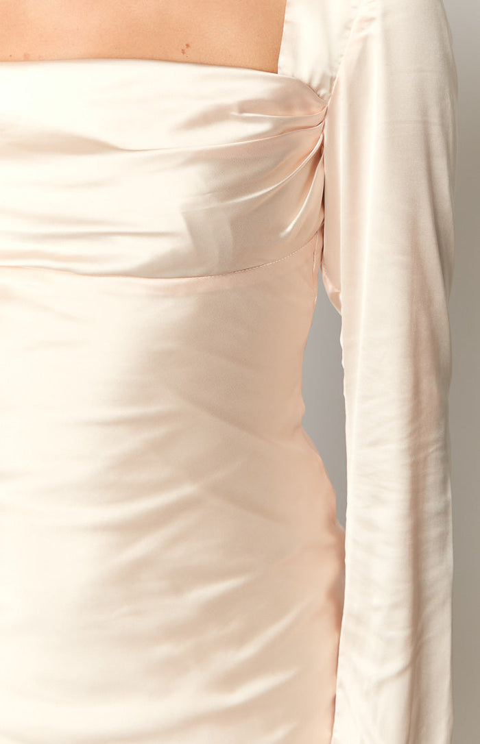 Close-up of the ruched detail at the square neckline and the long sleeve of a cream satin dress