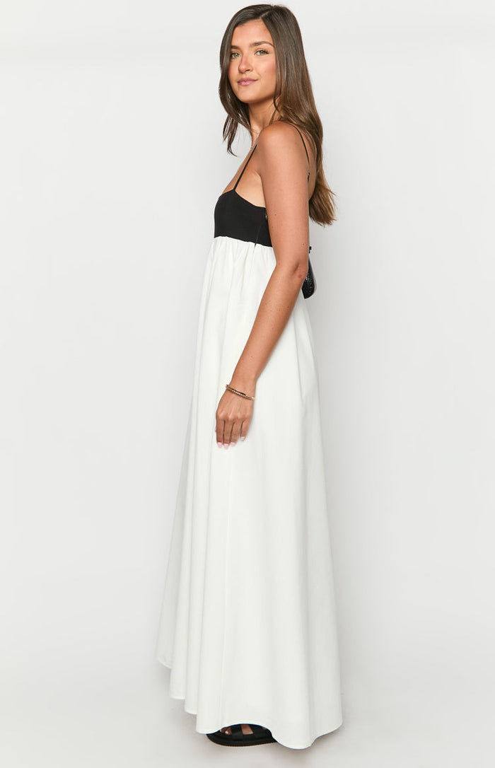 Side view of a black and white contrast maxi dress with thin spaghetti straps and a flowy white skirt