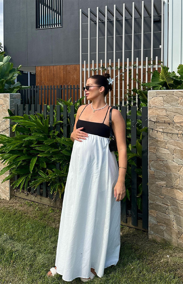 Side view of a black and white contrast maxi dress with thin spaghetti straps and a flowy white skirt