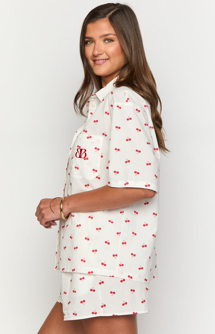 Side view of white pajama shorts with red cherry print, peeking out from under a matching shirt