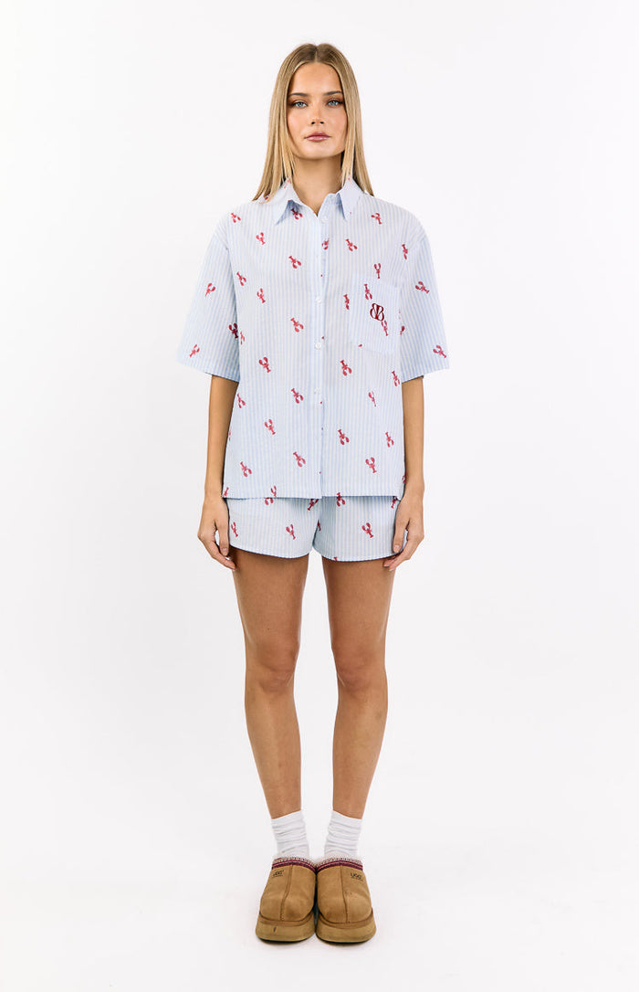 Front view of a light blue and white striped pajama shirt with red lobster print, collared neckline, button-front, and chest pocket with BB logo