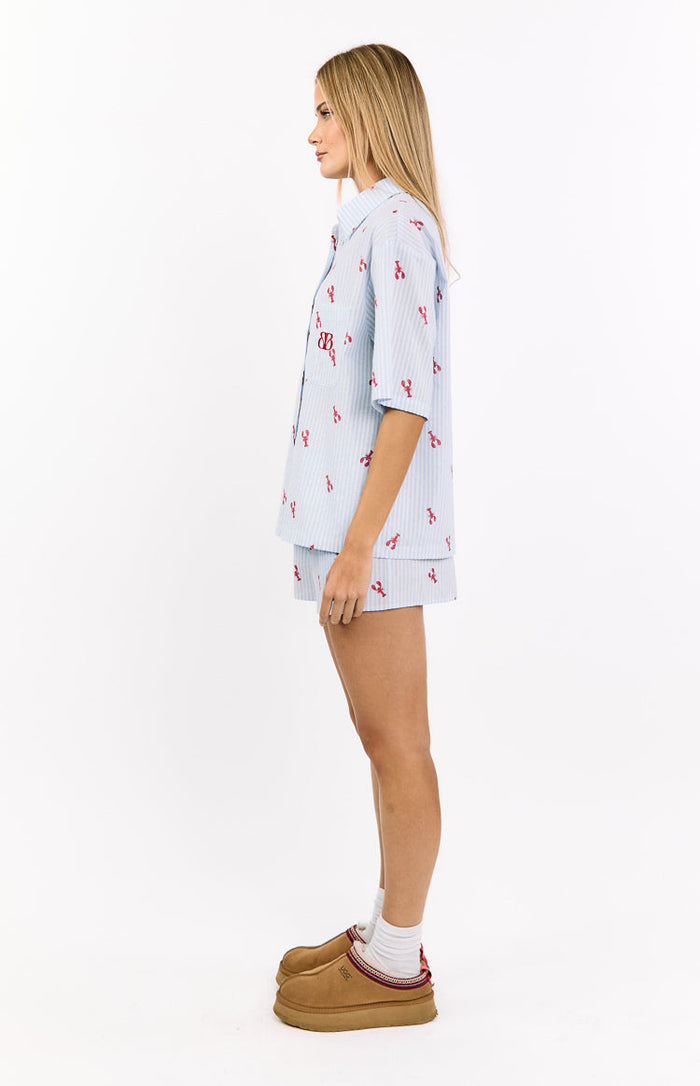 Side view of a light blue striped pajama shirt with red lobster print, short sleeves, and a BB monogram on the chest pocket