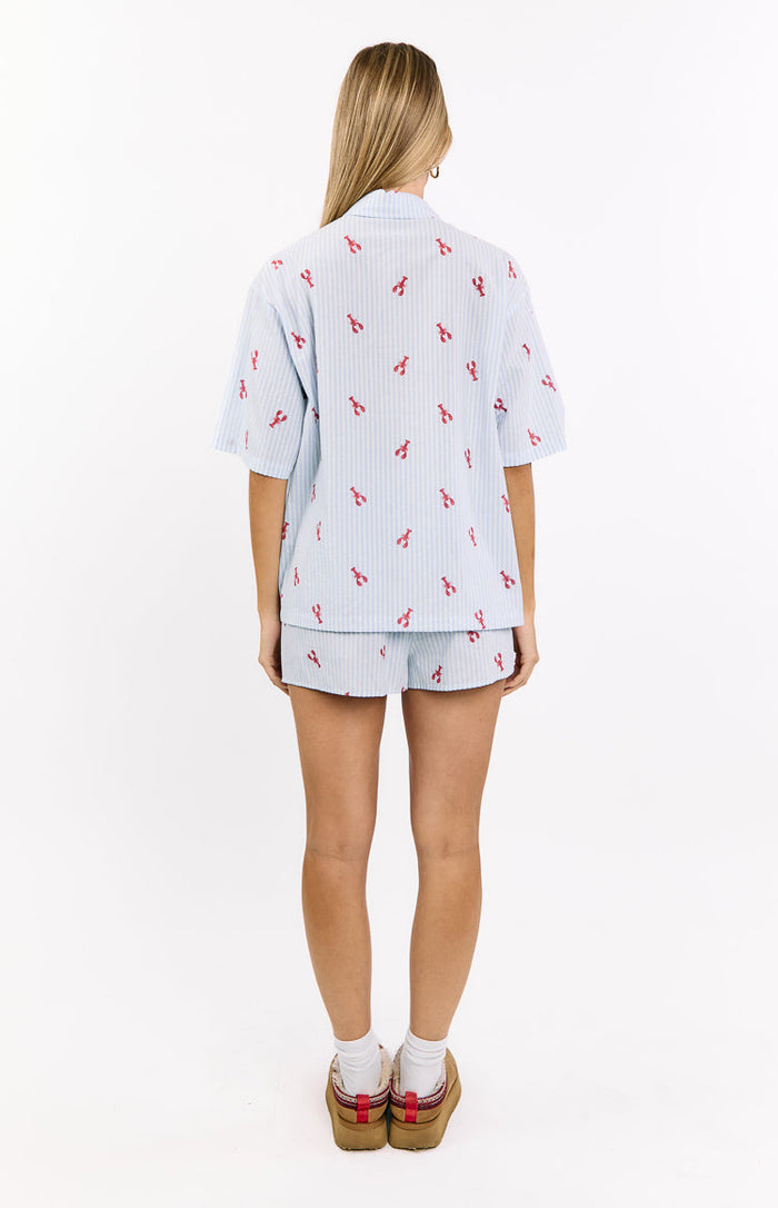 Rear view of a light blue striped pajama shirt with a relaxed fit, short sleeves, and all-over red lobster print