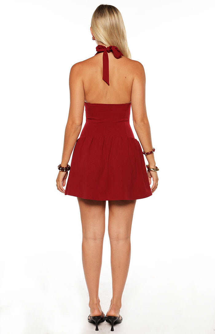 Rear view of a burgundy halter neck mini dress with a tied bow at the back and a gathered skirt