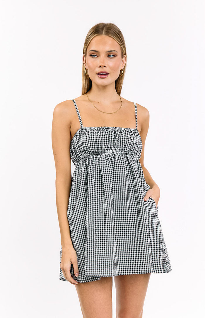 Front view of a black gingham mini dress with a shirred bodice, square neckline, and gathered skirt with pockets