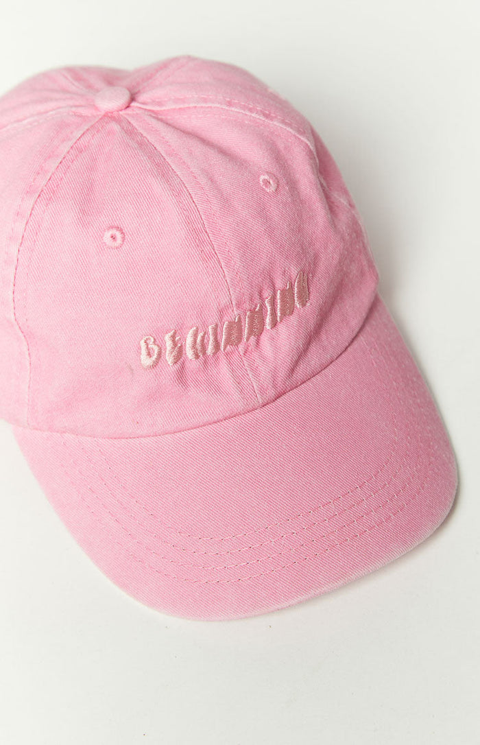 Close-up of the front of a pink washed cap showing light pink embroidered text and brim stitching