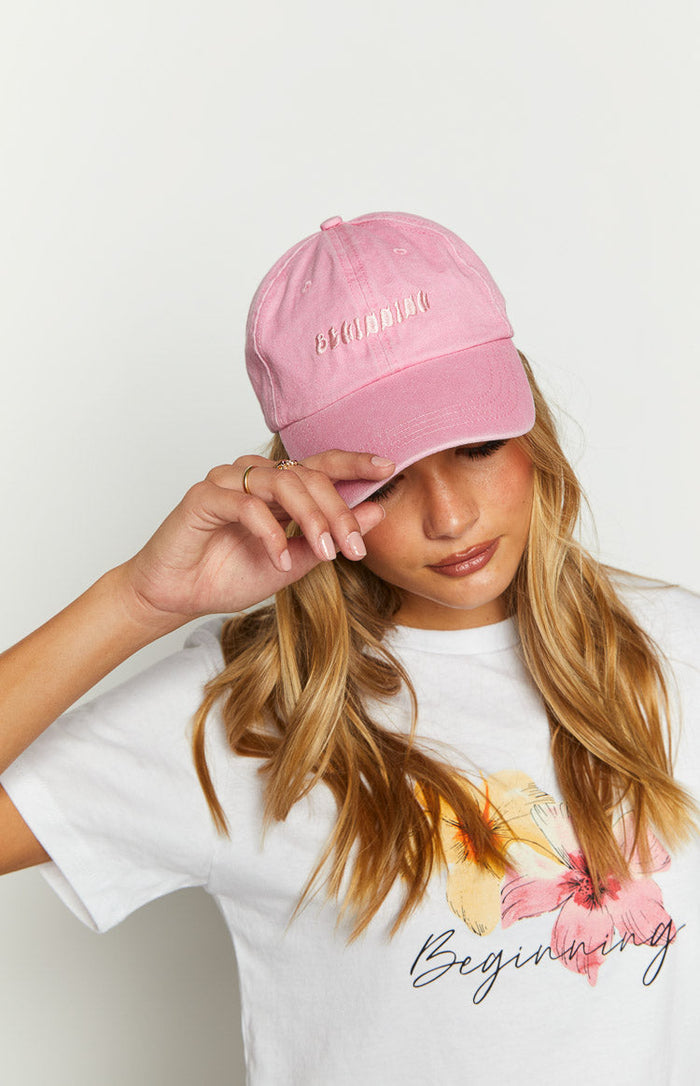 Close-up of the pink washed cap showing the embroidered "BEGINNING" text on the front and the distressed brim