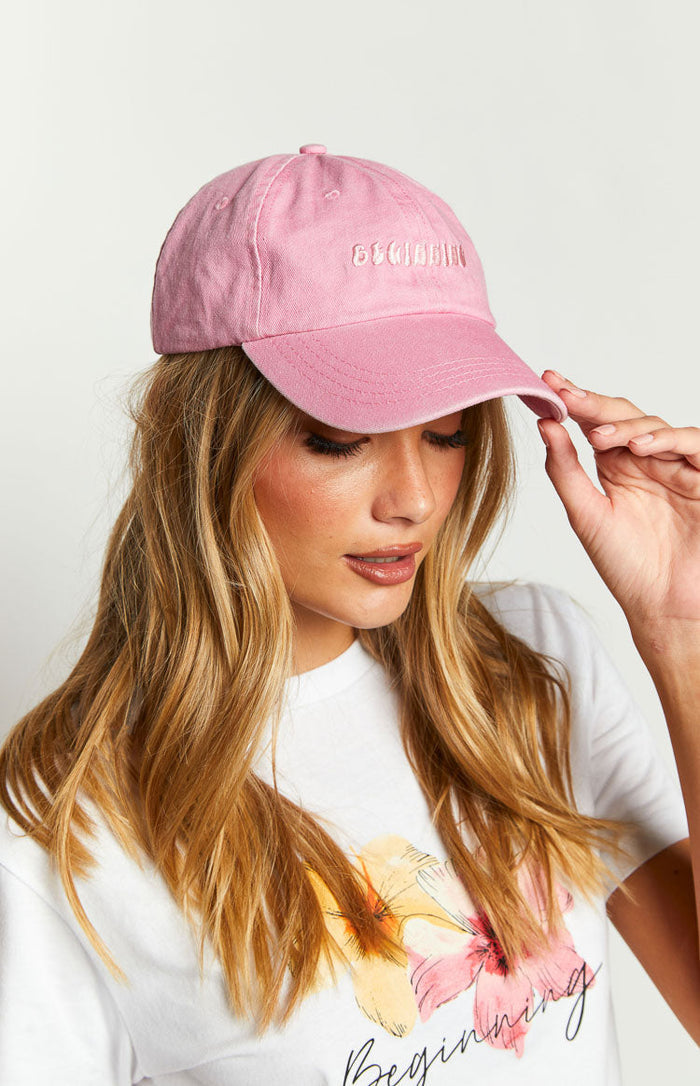 Close-up of a pink washed cap with embroidered text on the front and a curved brim