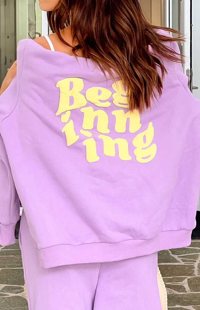 Rear view of a purple hoodie with yellow raised "Beginning" text on the back, worn off-shoulder