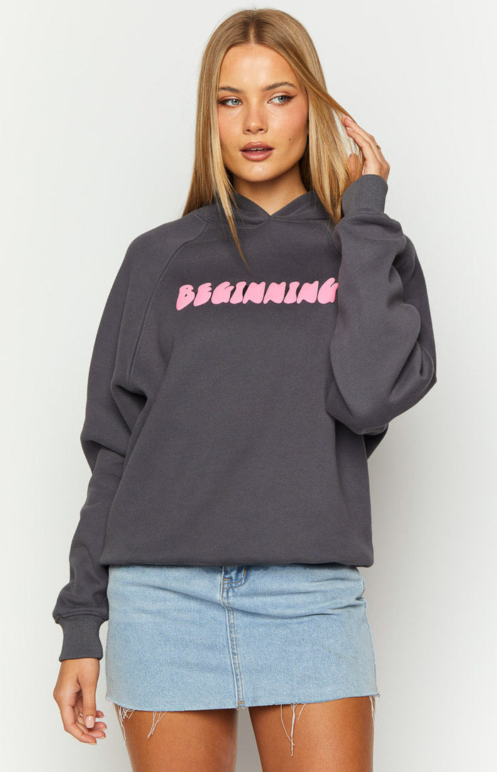 Slate grey relaxed fit hoodie with pink "BEGINNING" text across the chest, raglan sleeves, and ribbed cuffs