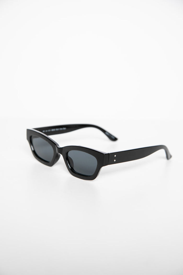Side view of black slimline sunglasses with dark lenses and two silver dots on the temples