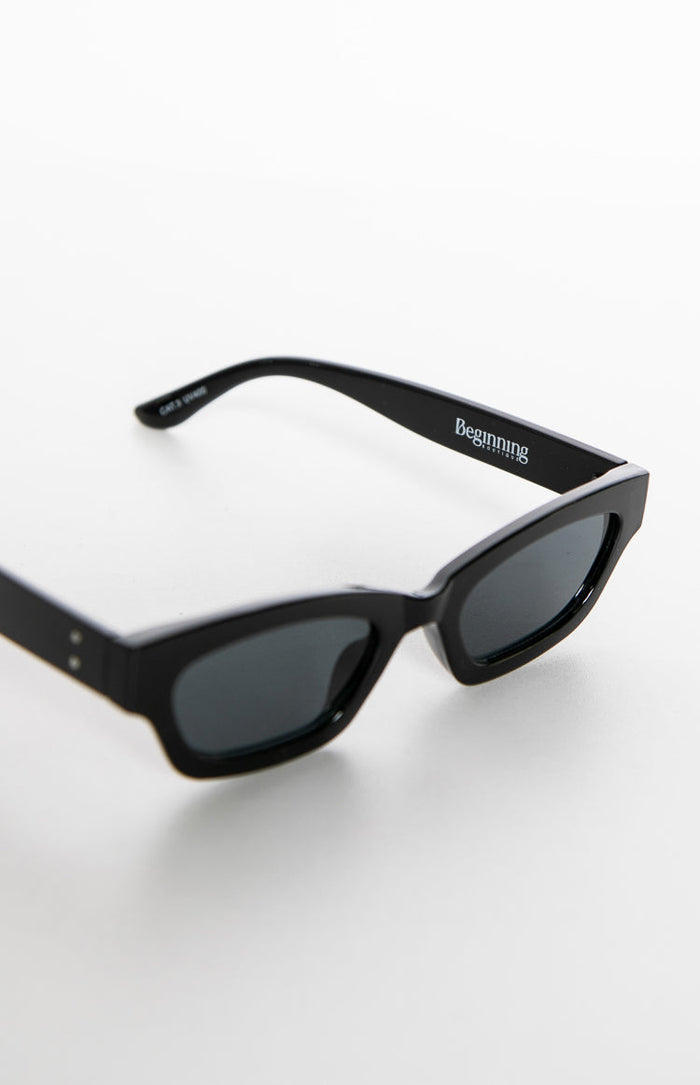 Close-up of the right arm of black slimline sunglasses, showing the white 'Beginning Boutique' logo