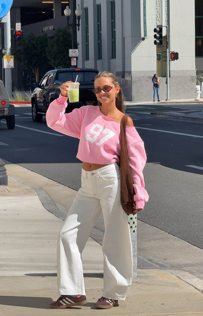 Front view of a pink off-shoulder cropped sweater featuring a large white '97' graphic on the chest