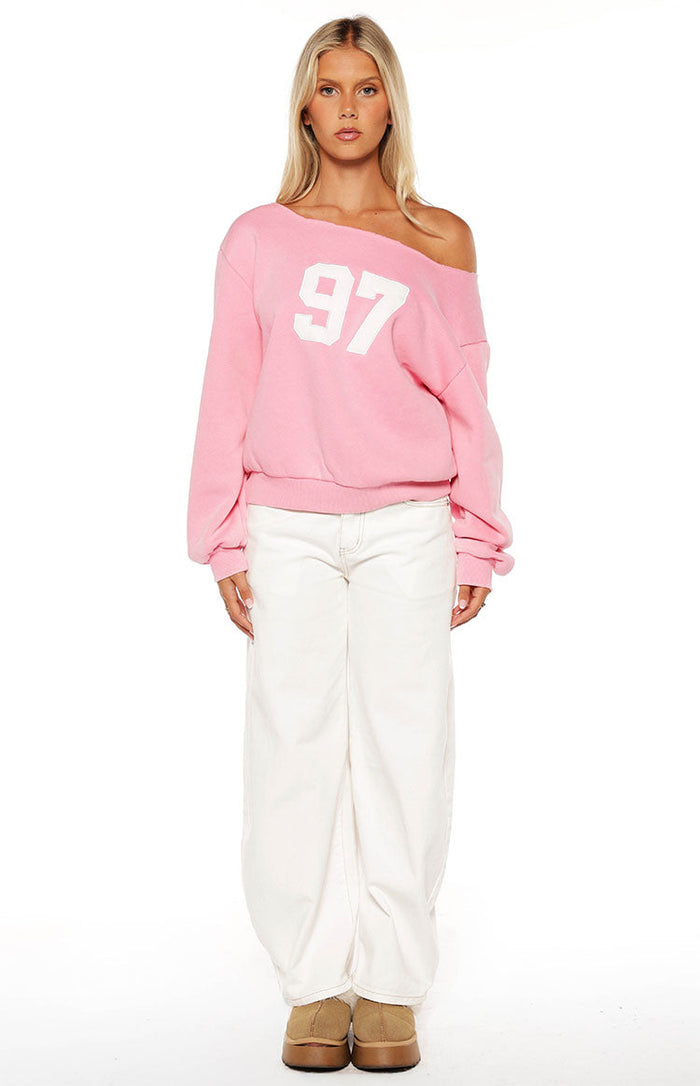 Front view of a pink wash off shoulder sweater with white '97' graphic and long cuffed sleeves