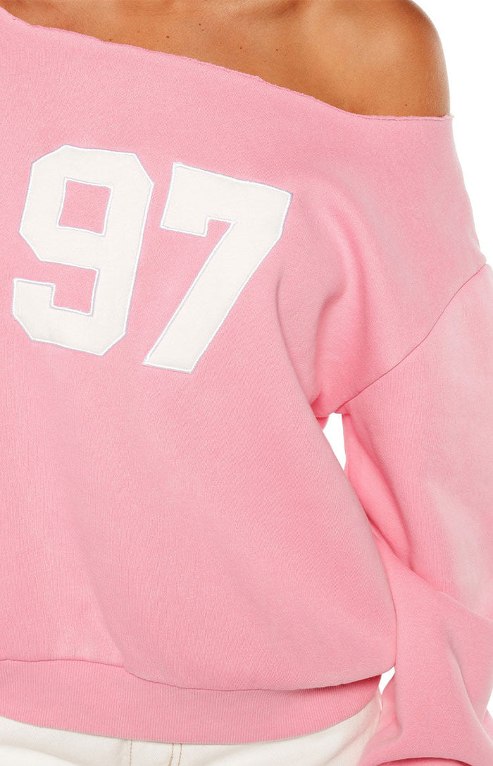 Close-up of the pink off-shoulder sweater showing the white '97' graphic and raw edge neckline