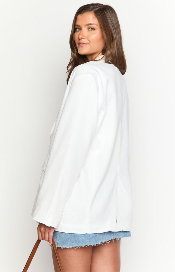 Three-quarter rear view of a white linen blend blazer with long sleeves and a relaxed, oversized fit