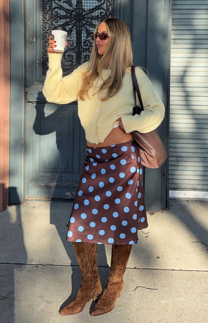 Angled front view of a brown midi skirt with large blue polka dots, showing its flowy satin-like drape