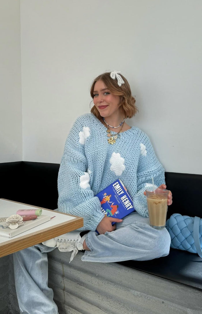 Light blue chunky knit sweater with white cloud appliques, wide crew neck, and relaxed oversized fit