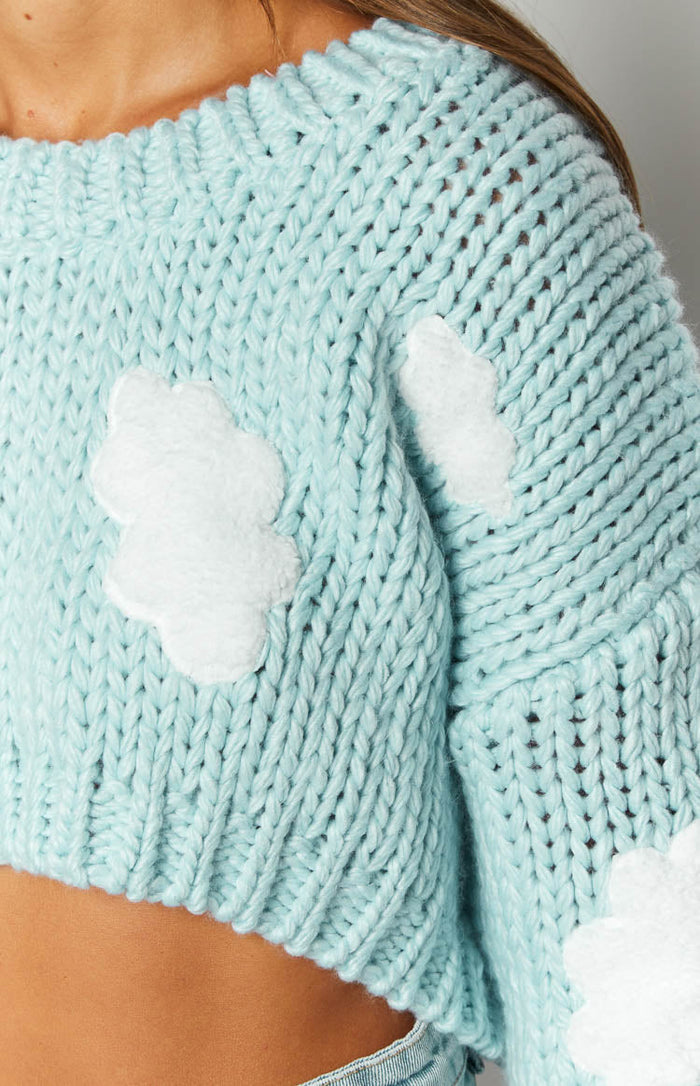 Textured close-up of the light blue chunky knit sweater showing the white cloud appliques on the body and sleeve