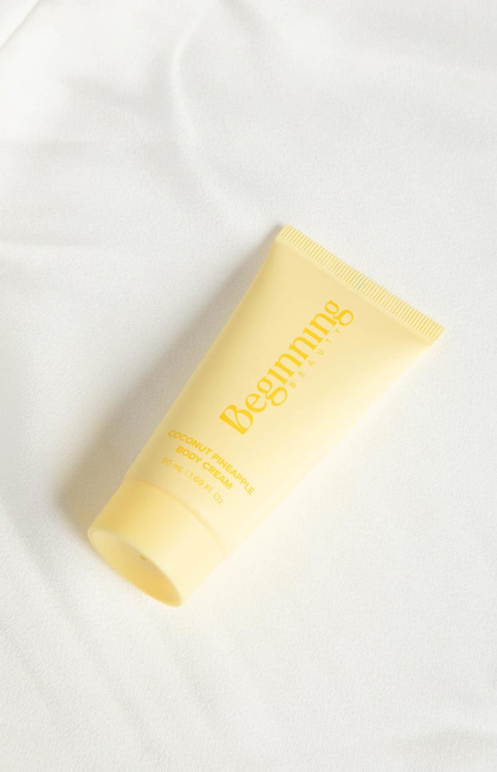Angled view of a light yellow body cream tube with 'Coconut Pineapple Body Cream' label