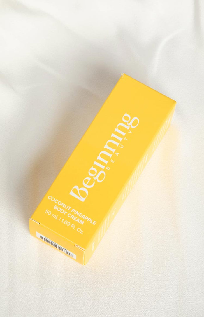 Angled view of a yellow rectangular box for coconut pineapple body cream, showing the front label, side branding, and barcode