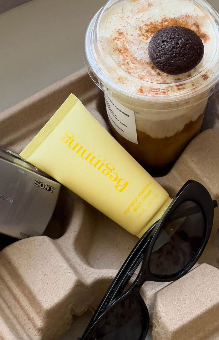 Angled view of a matte yellow squeeze tube of body cream with orange text for product name and volume