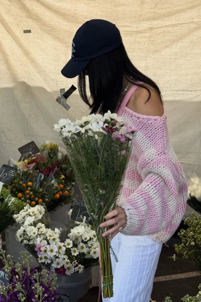 Side view of a pink striped chunky knit sweater with an off-shoulder neckline and relaxed long sleeves