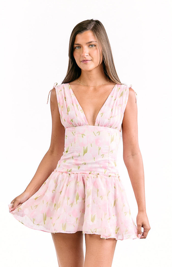 Front view of a pink floral mini dress with a deep V-neck, tie-shoulder straps, and a ruffled hem