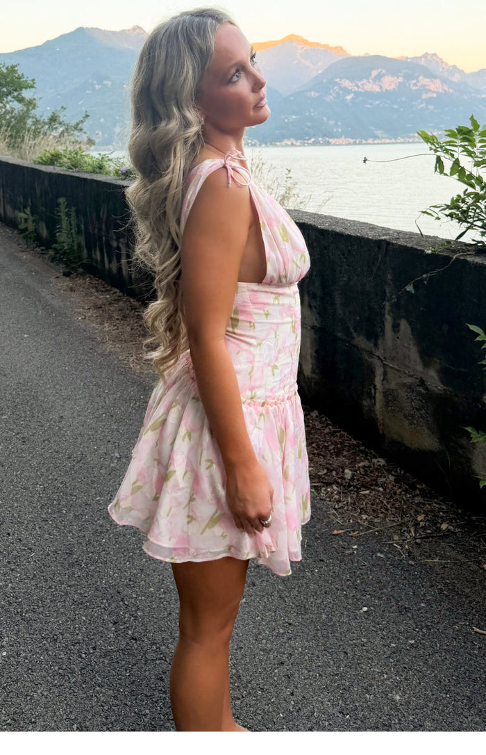 Side view of a pink floral mini dress with tie-shoulder straps, deep armholes, and a ruched waist leading to a flowy tiered s