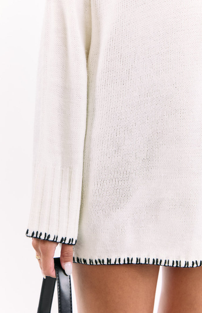 Ribbed cuff and hem of a cream knit sweater dress with black contrast stitching
