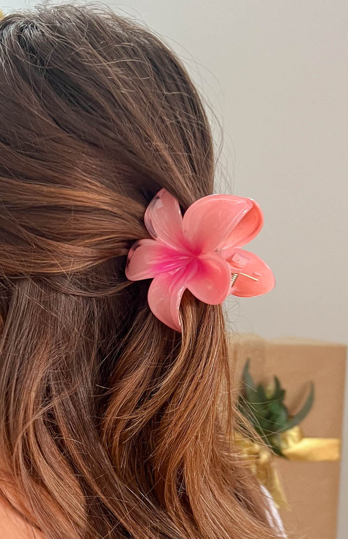 Side view of a translucent pink frangipani flower hair clip with a vibrant pink center, worn in brown hair