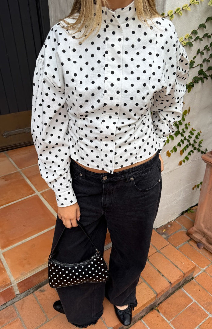 Front view of a white polka dot jacket with a high stand collar, puffed long sleeves, and a cropped fitted waist