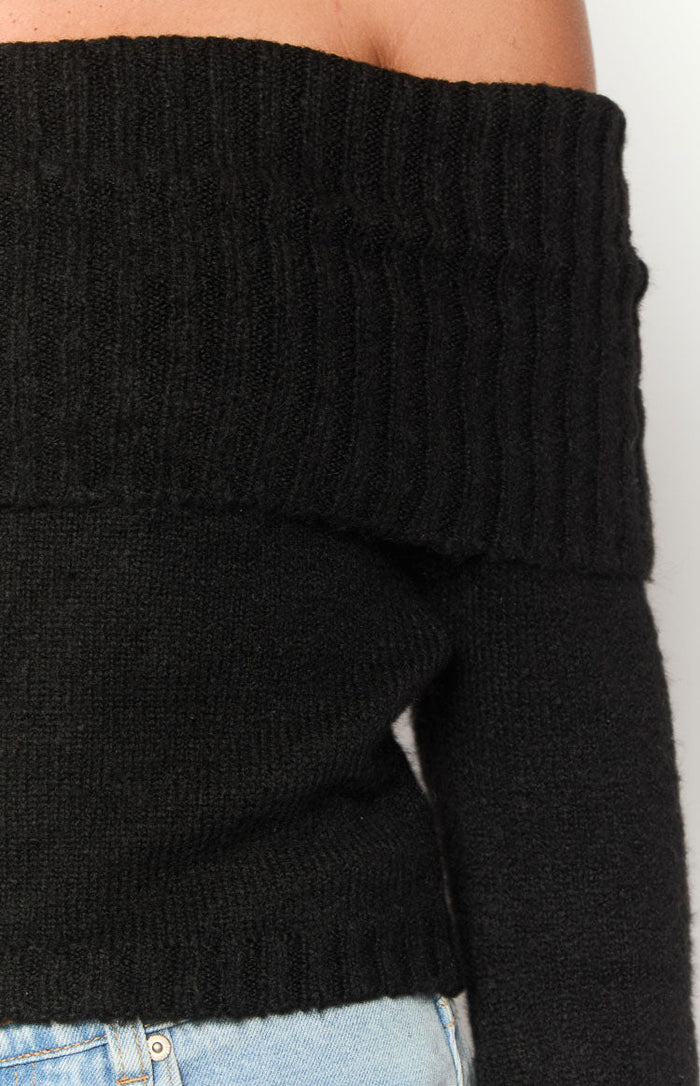 Close-up of the black off-shoulder sweater showing the ribbed fold-over neckline and soft knit texture