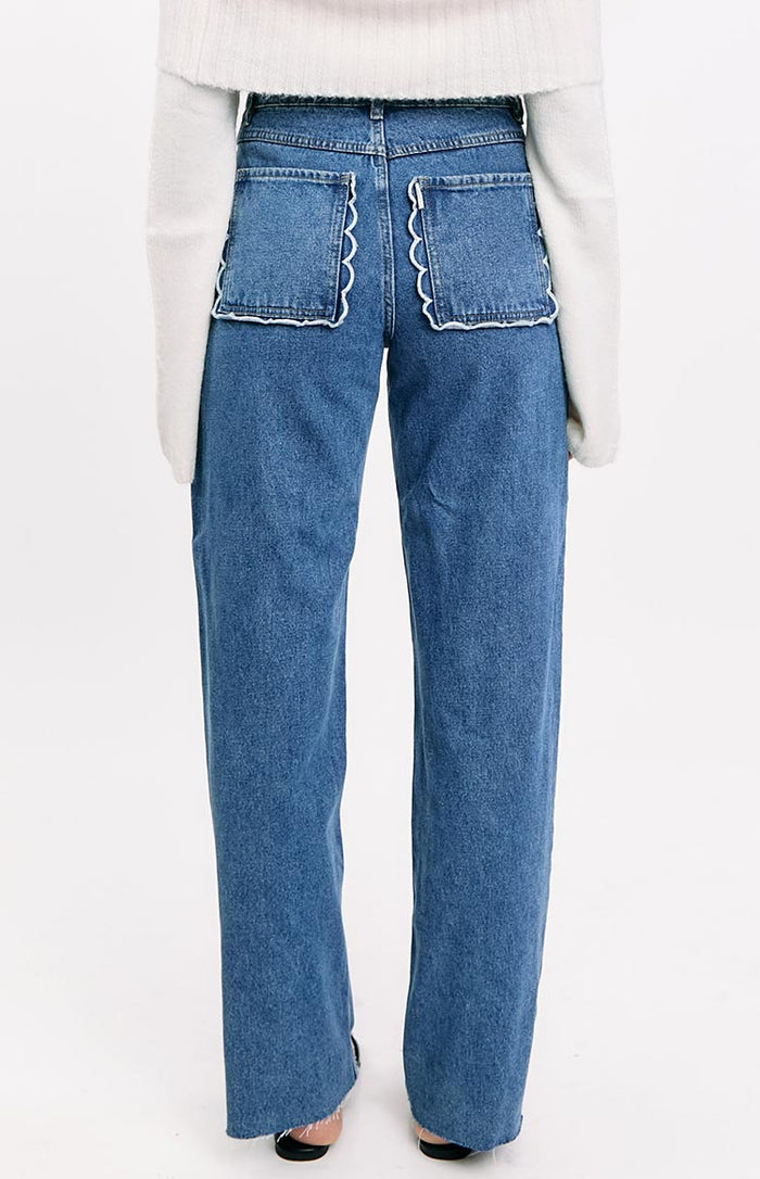 Rear view of mid-wash denim jeans with white scallop trim on the back patch pockets