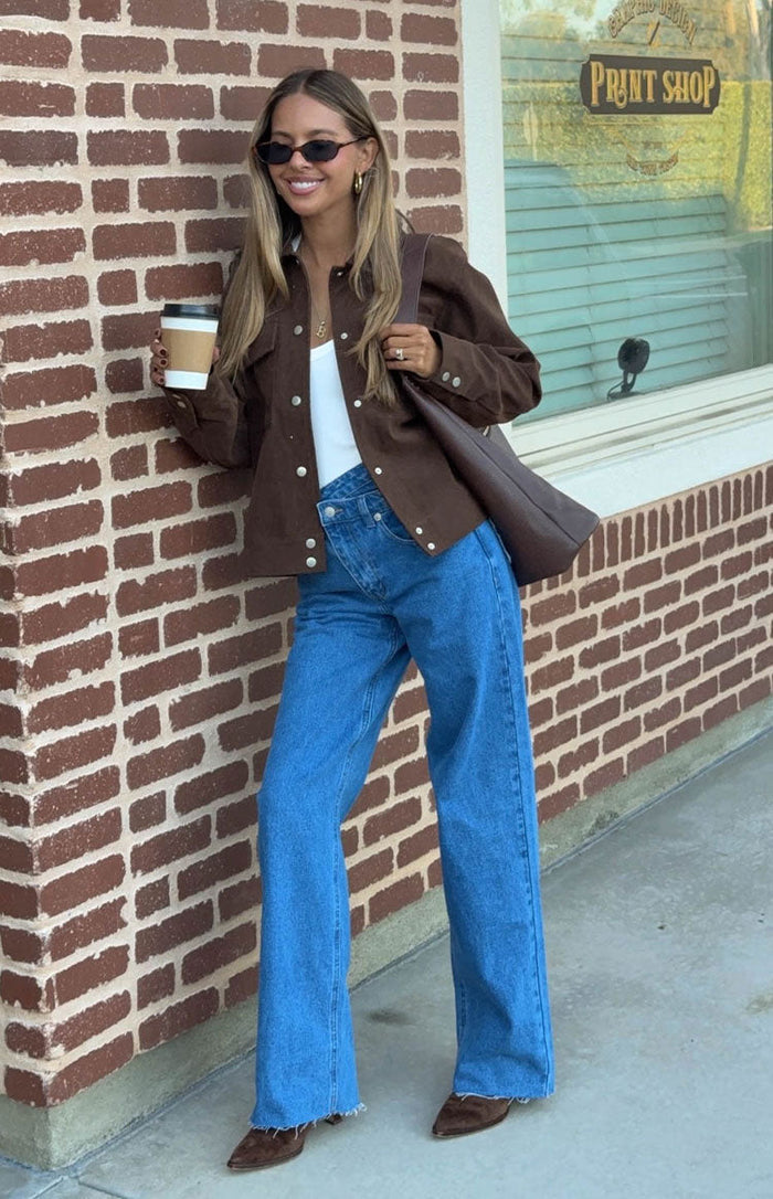 Mid wash blue wide-leg jeans with an uneven crossover waist and frayed hems