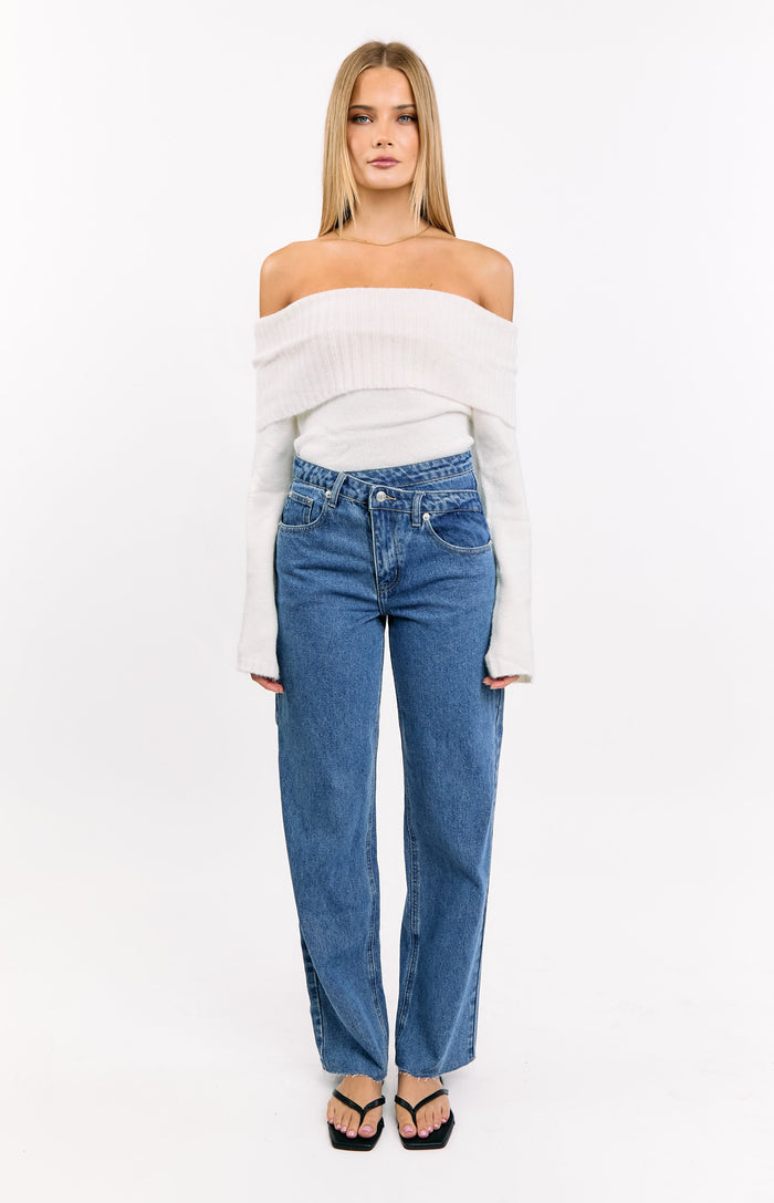 Front view of mid wash blue straight leg jeans with an uneven crossover waistline