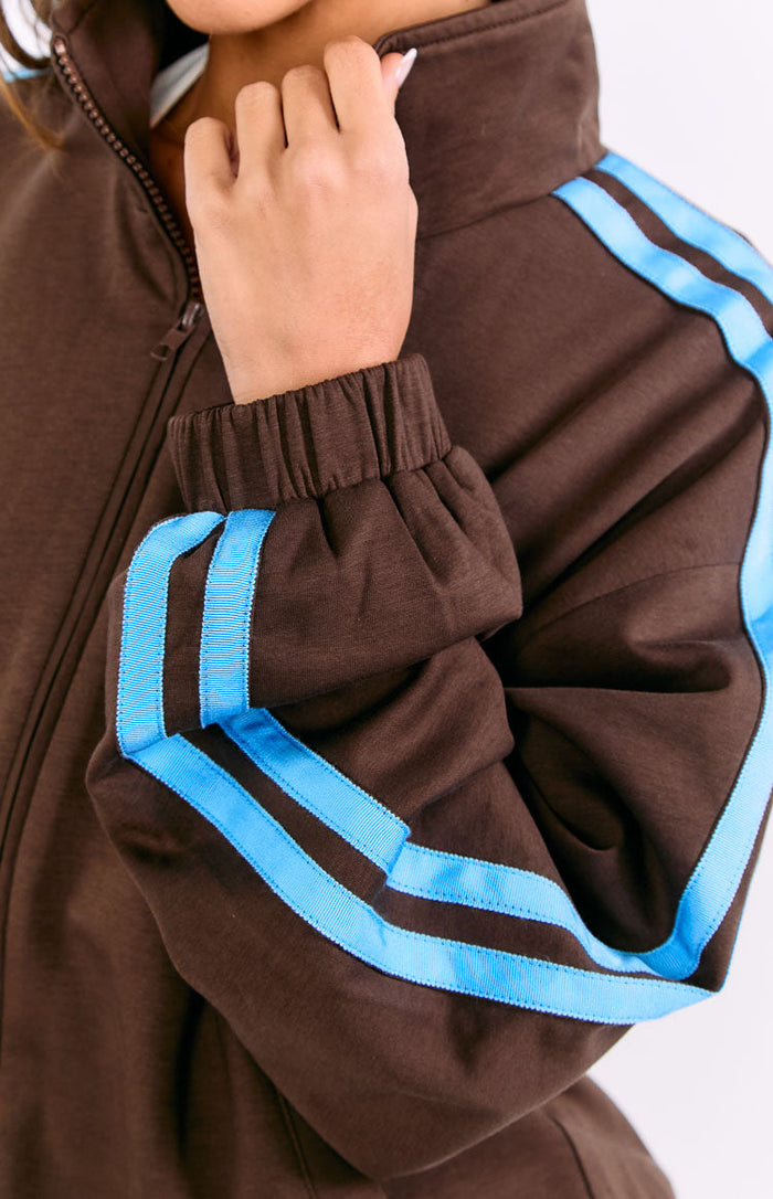 Close-up of the chocolate brown jacket's ribbed cuff, light blue sleeve stripes, and zipped stand collar