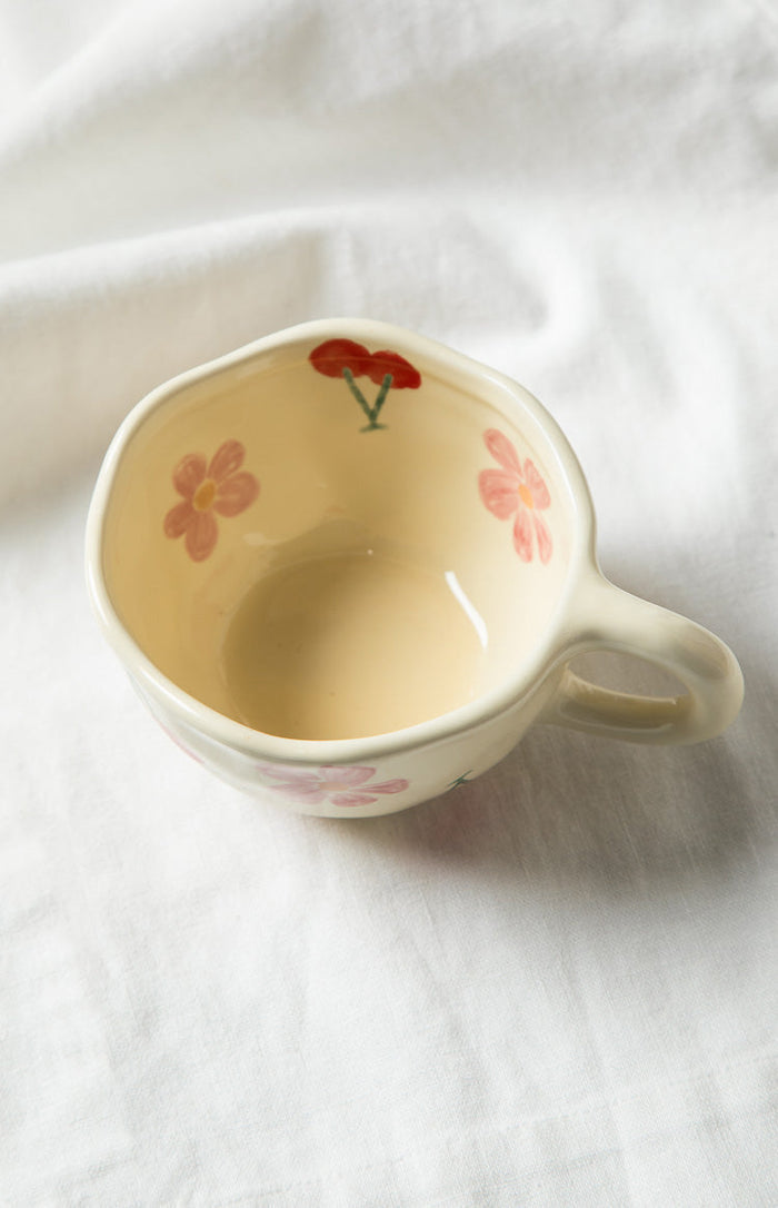 Top-down view of a cream mug with pink floral patterns and a red cherry design on the inside rim