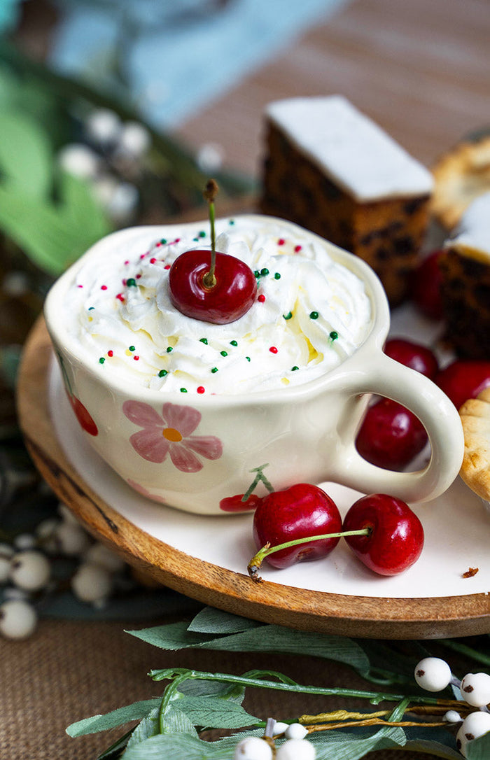 Cream ceramic mug with a pink flower and red cherry design on the side, showing the handle