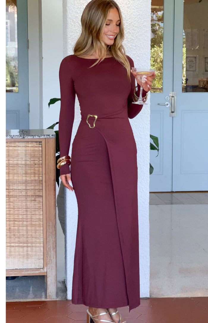 Burgundy long sleeve maxi dress with a boat neck and gold buckle detail at the wrap waist