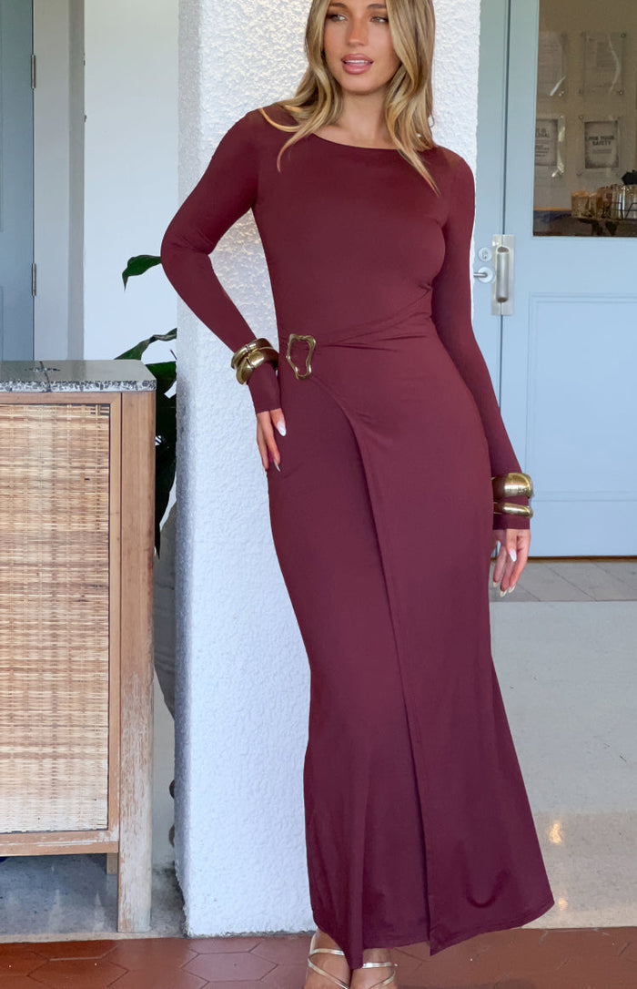 Full length view of a burgundy long sleeve maxi dress with a wide scoop neck and wrap skirt with a gold buckle