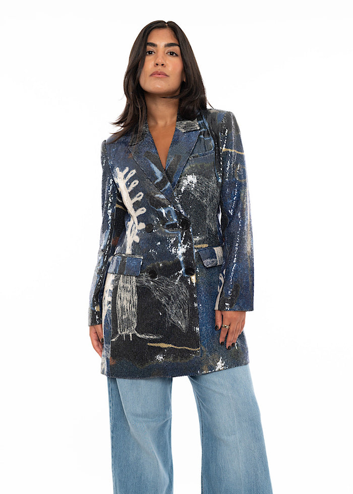 A model wearing a Blue and Black Sequin Blazer. With two front pockets and buttons to fasten. Styled with light blue straight leg jeans.