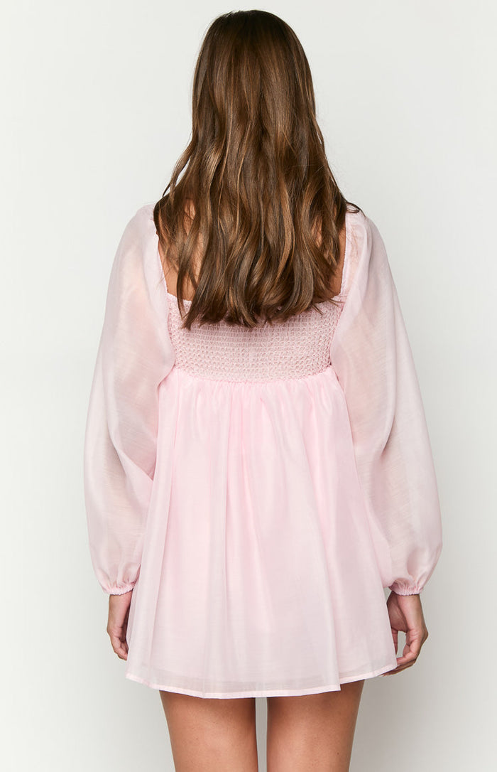 Rear view of the pink mini dress showing the shirred back bodice, square neckline, and sheer long sleeves