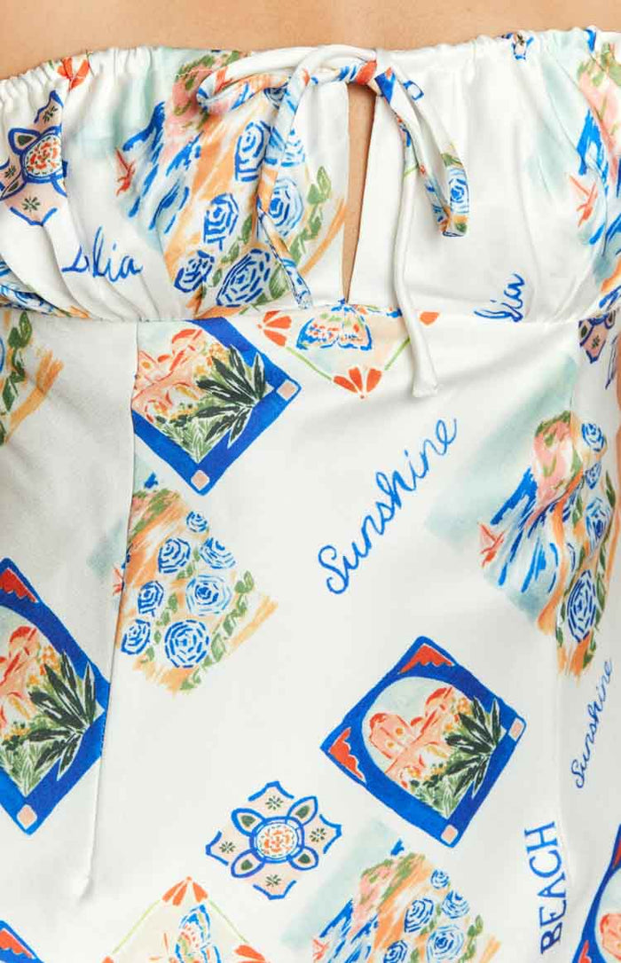 Close-up of the white strapless mini dress showing the tie-front keyhole and the colourful Italia print with 'Sunshine' text and blue and orange floral motifs
