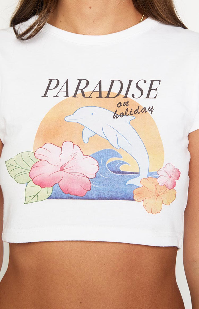 Close-up of the graphic print on a white cropped tee featuring a dolphin, waves, sun, and hibiscus flowers with "PARADISE on holiday" text