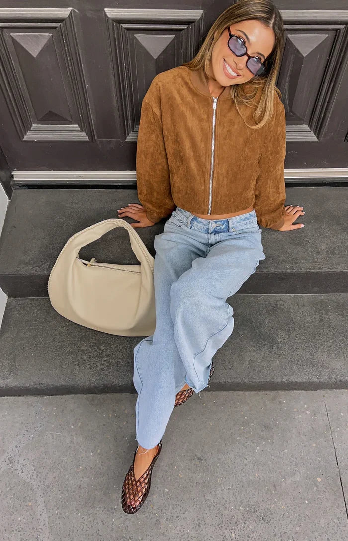 Front view of a cropped brown suedette bomber jacket with a relaxed fit, silver full-zip, ribbed collar, and cuffed long slee