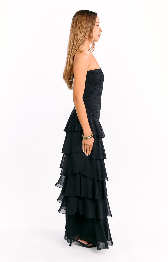 Side view of a black strapless maxi dress with a smocked bodice and tiered ruffle skirt